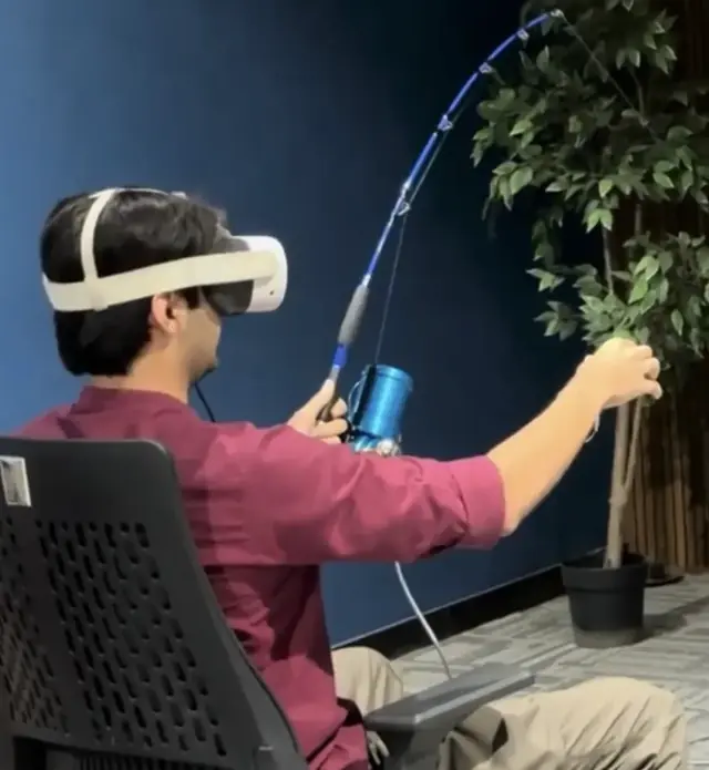 A player in a VR headset holding a fishing rod with a reel